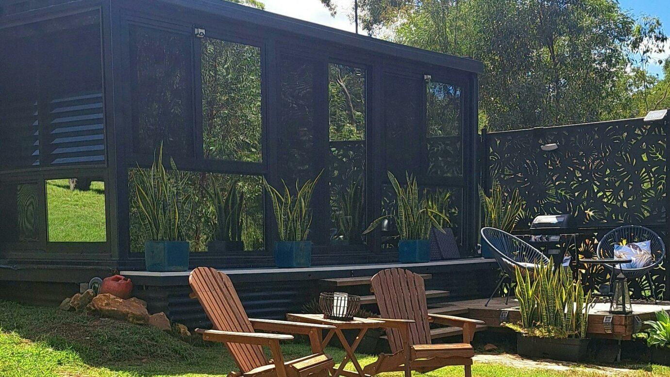 a image of a container conversion tiny home set amongst the trees. With firepit and seating