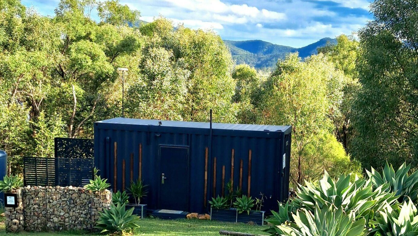 a black container converted into a tiny home with a green bush setting and mountains beyond