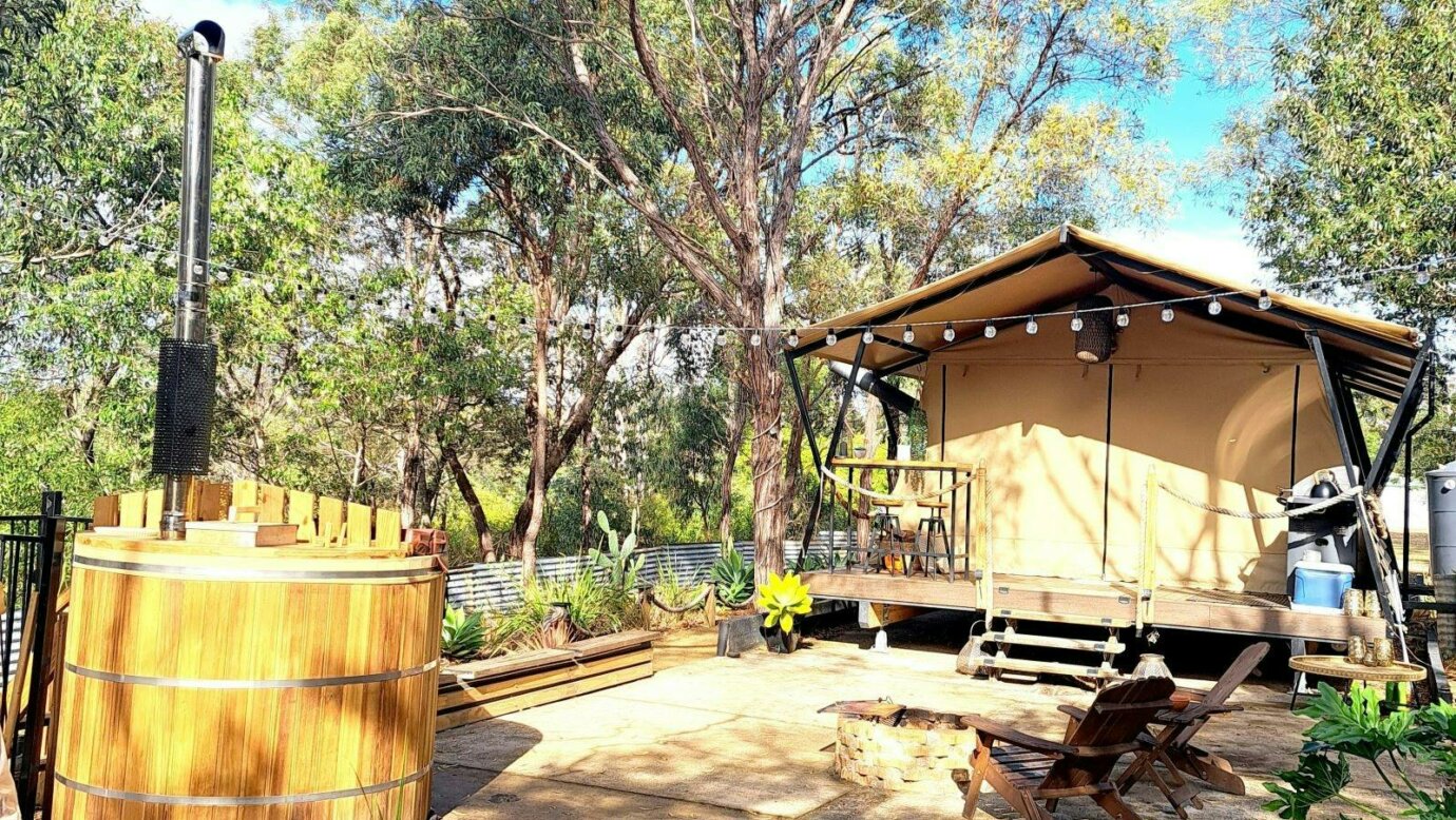 sarafi canvas tent set in bush with a round wooden hot tub with chimmney in foreground