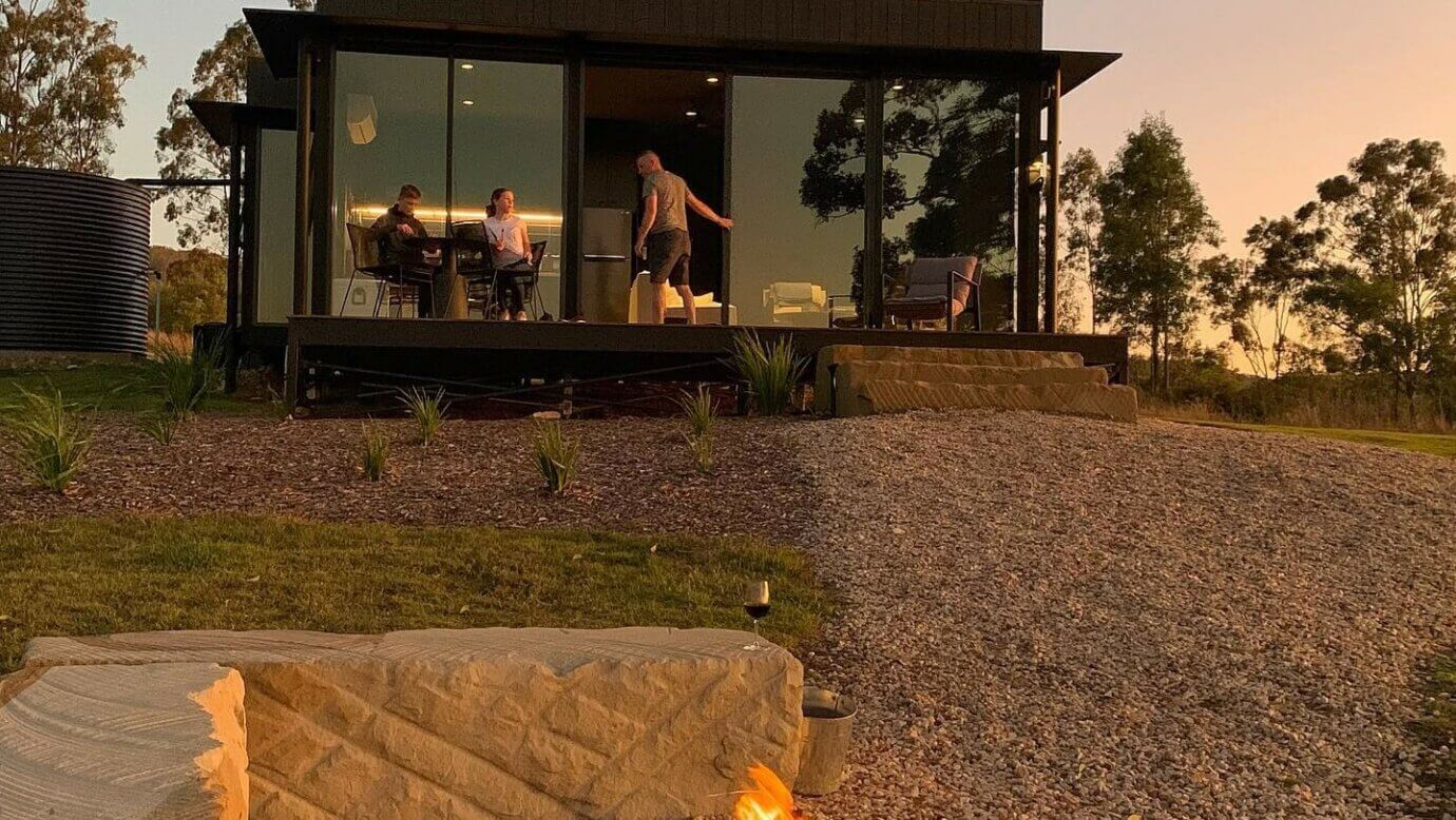 Three people enjoying sustainable travel, standing on the deck of eco accomodation at sunset.