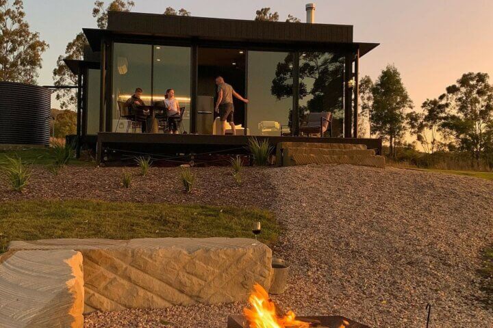 Three people enjoying sustainable travel, standing on the deck of eco accomodation at sunset.