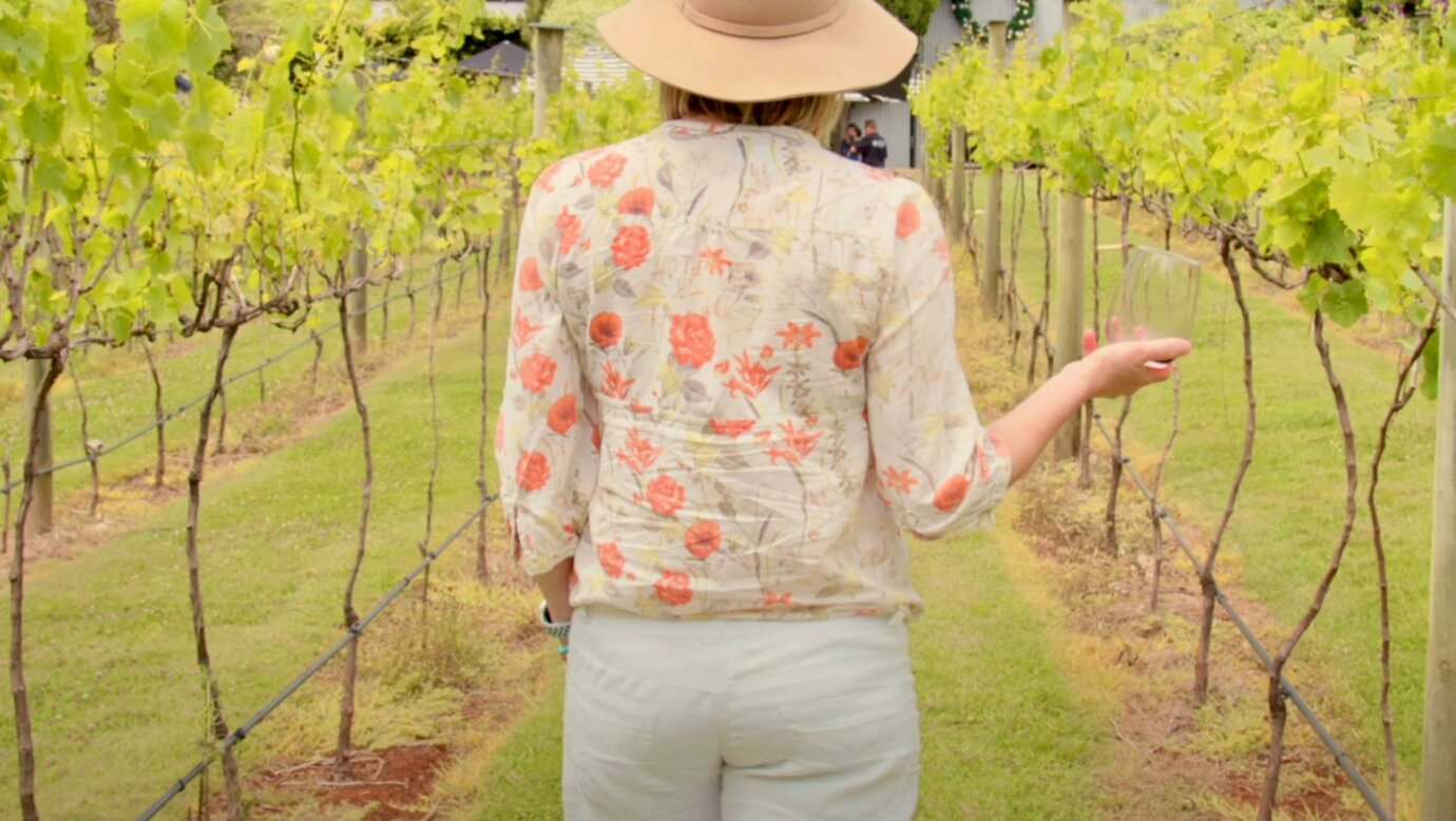 A women holding a glass of white wine walking through the vineyard at Witches Falls Winery