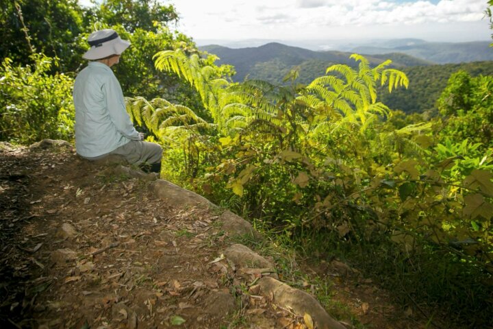 Walker sits on rock ledge looking over wideranging view of mountains in distance.