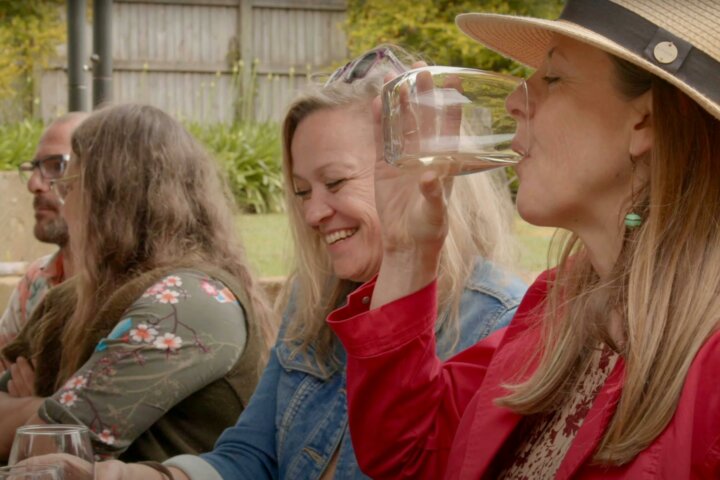 A women sipping a glass of white wine with a group of friends at Witches Falls Winery