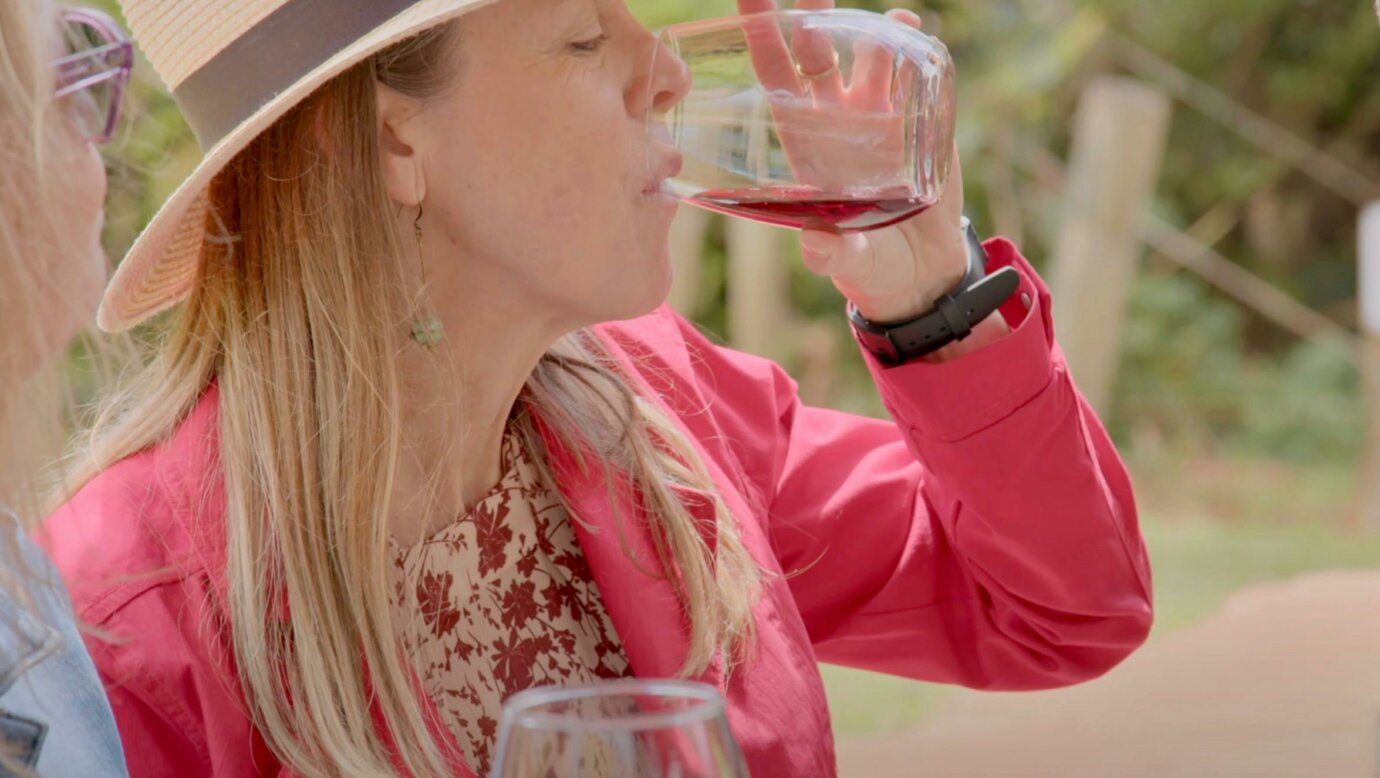 A women wearing a red jacket and straw hat sipping a glass of red wine at Witches Fall Winery