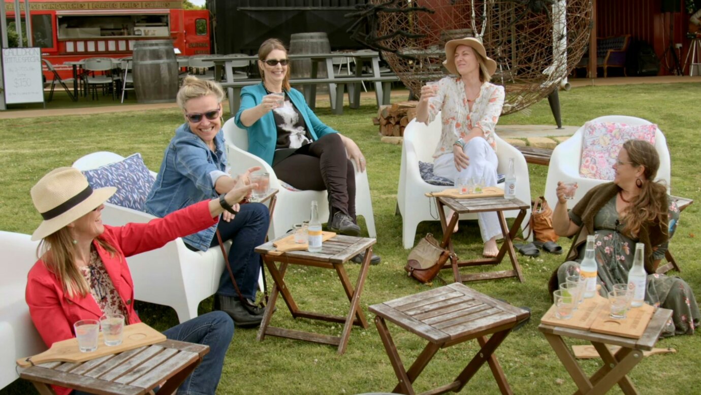 Group of women sitting on the lawn outside Cauldron Distillery sipping gin