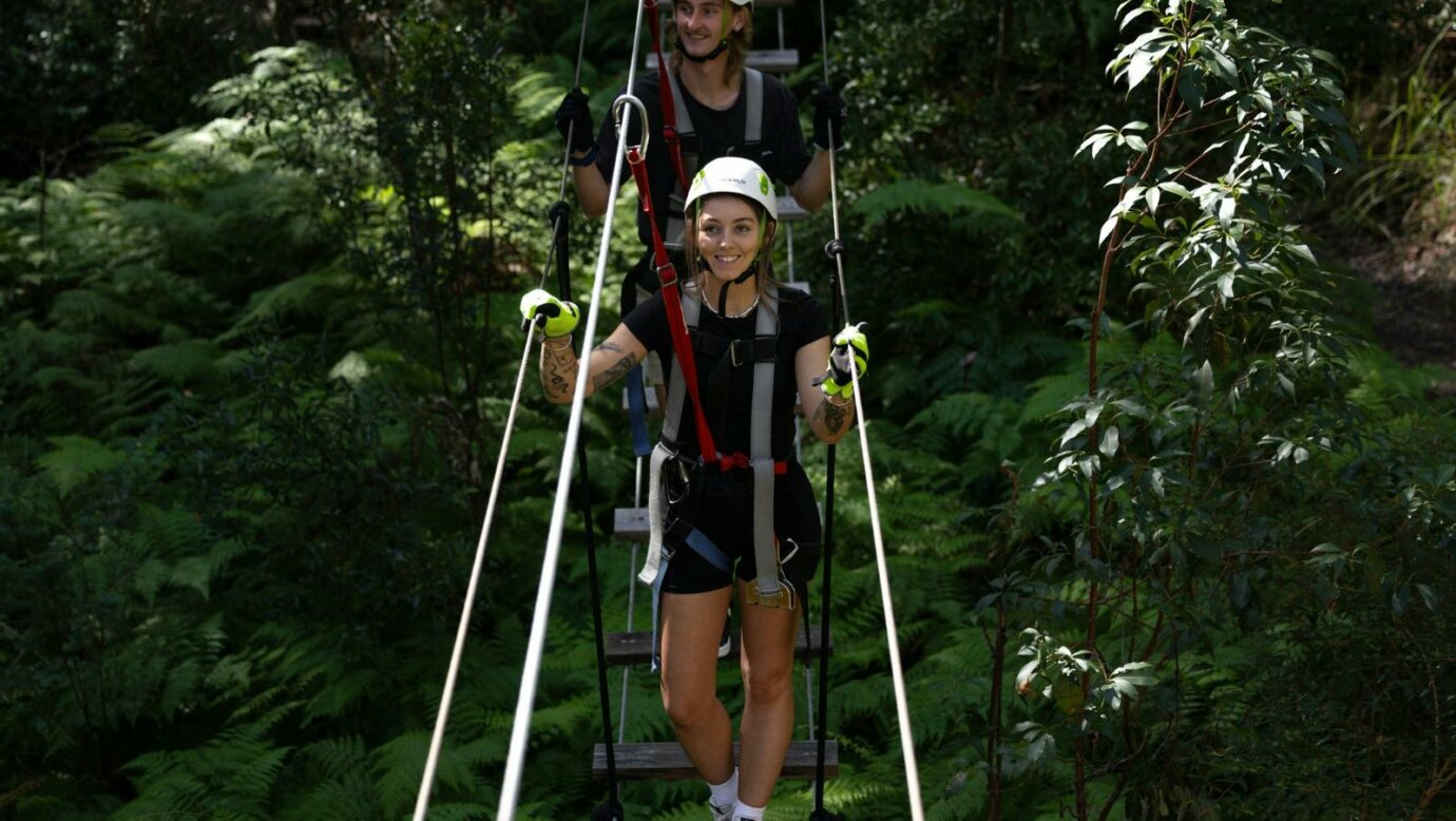 2 people walking across a suspension bridge smiling.